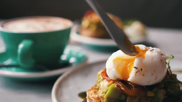 Female Hands Cutting Poached Egg Avocado Mashed Toast Cup with Coffee on Background