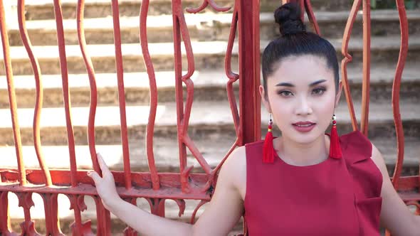 Beautiful Asian Woman In Red Suit Pose At Red Metal Fence alt