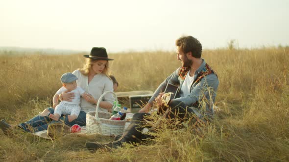 Man Playing Guitar for Family During Picnic