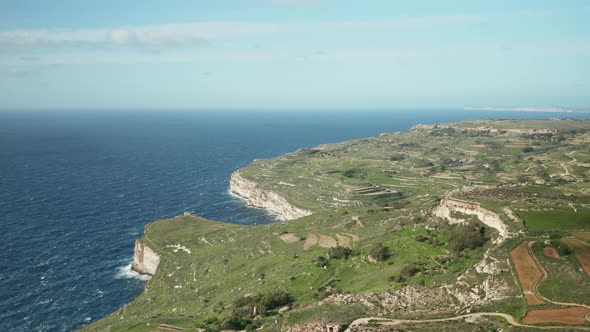 AERIAL: Vast Blue Mediterranean Sea Wash Dingli Cliffs with Great Green Scenery on Hill