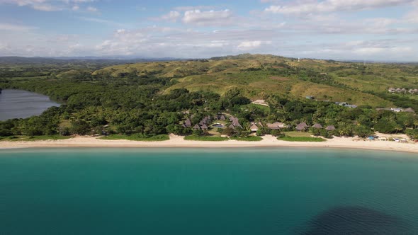 Drone flying along the coastline of Natadola Beach in Fiji looking at the resorts and green mountain alt