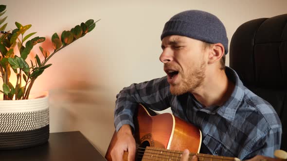 Male singer sings song and plays guitar at home in front of laptop, learns new music composition. alt