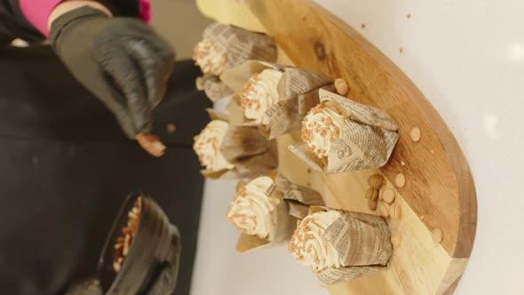 Hands finishing up decorating muffins with walnuts. Vertical, gimbal, close up alt