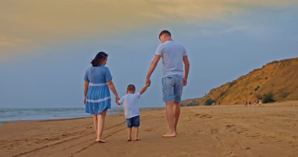 Married Couple with a Child are Walking By the Sea Holding the Baby By the Hands and Lifting Him Up