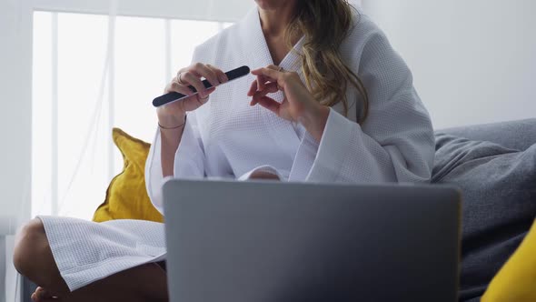 Woman at Home Files Nails on Couch Before Laptop