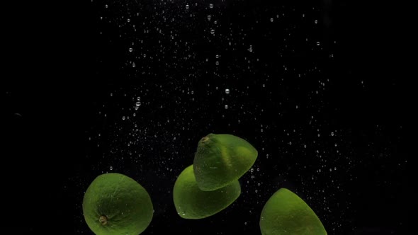 Slow Motion Green Lime Halves Falling Into Transparent Water on Black Background alt