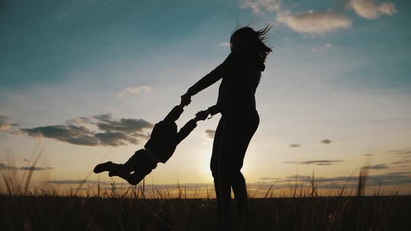Silhouettes Happy Young Mother and Son Who Play Outdoors at Sunset. Concept of Motherhood alt