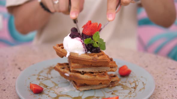 Female Hands Cutting a Stack of Belgian Waffles Topped with Ice Cream with Fork and Knife alt