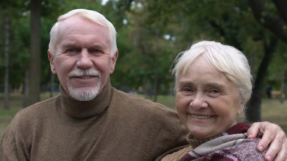 Smiling Mature Couple Sitting on Bench in Park and Hugging, Social Security