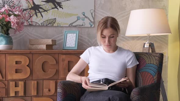 Young woman reading book in cozy living room, turning page, learning, studying, education