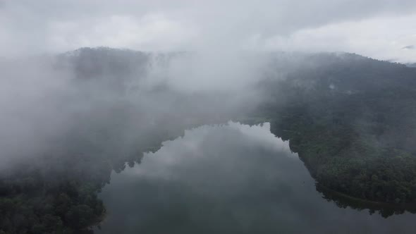 Aerial fly away low cloud of lake at tropical rainforest alt