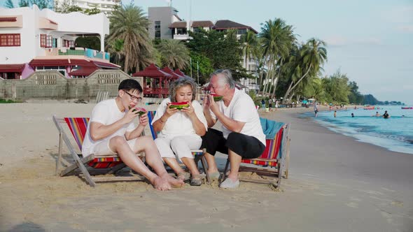 Happy couple senior elderly retirement and son eating watermelon on the beach together alt