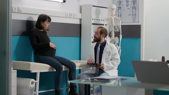 Male Doctor Consulting Pregnant Woman and Using Digital Tablet alt