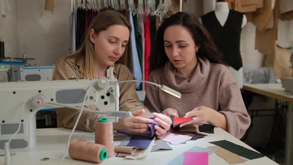 Two femail fashion designers looking at samples of sketches in a sewing workshop studio alt