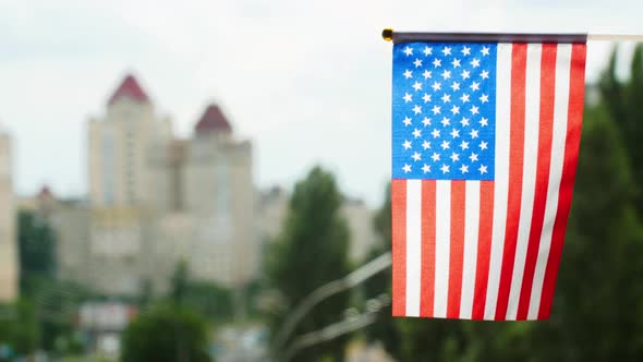 Flag of the United States of America set against blue sky, city street and buildings. Stars