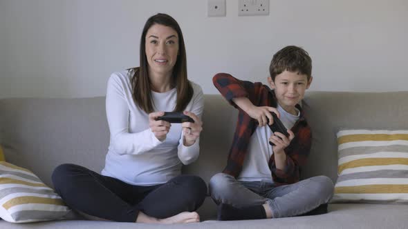 Mother and son playing with gaming consoles sitting on couch