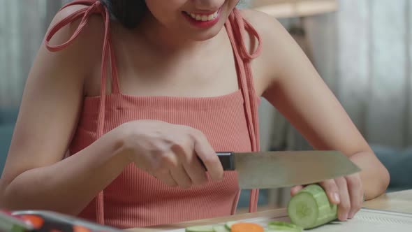 Close Up Of Smiling Asian Woman Enjoys Slicing The Cucumber At Home alt