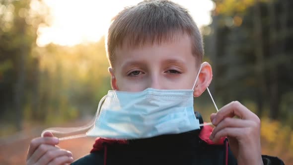 Child Boy Takes Off His Medical Mask Outdoors.