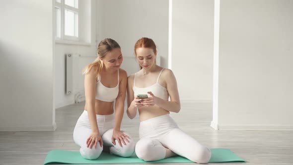 Two Slim Women in Sportswear Have Rest Using Smartphone Looking at Screen of Mobile Phone
