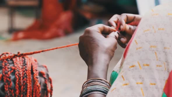African Woman Weaving African Braids with Red Kanekalon Outdoor Zanzibar Africa alt