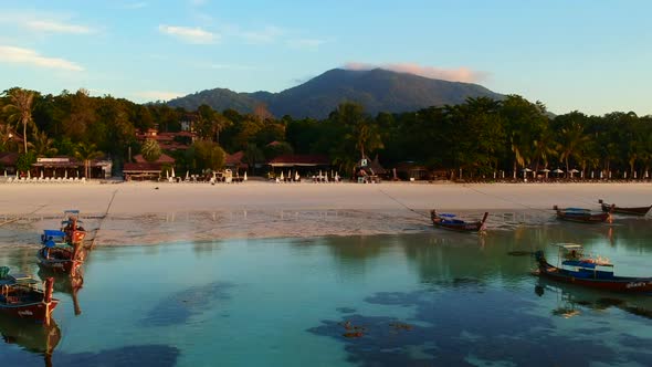An aerial shot of a white sand beach with boat and green forest in the background. alt