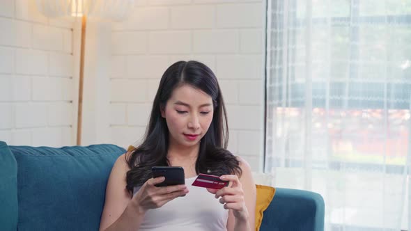 Young smiling Asian woman using smartphone buying online shopping by credit card. alt