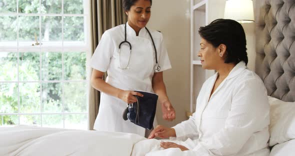 Female doctor measuring blood pressure of mature woman in bedroom 4k alt