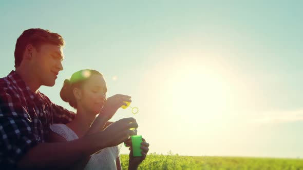 Romantic couple blowing bubbles in mustard field alt