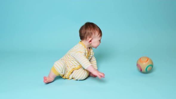 Happy toddler baby boy is playing with a ball on a studio blue background. Smiling child throws a ba