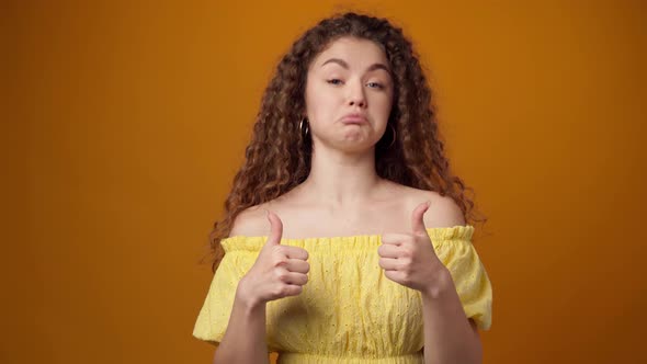 Young Curly Haired Woman Showing Thumbs Up Sign Against Yellow Background