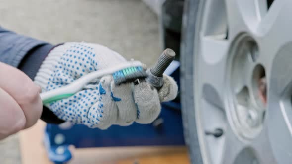 Hands of Mechanic Cleaning Car Wheel Bolt with Old Tooth Brush
