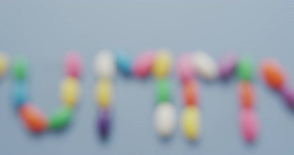 Video of overhead view of yummy text formed multi coloured sweets over blue background alt