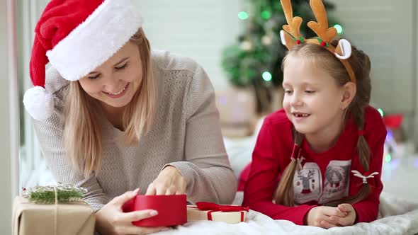 Mom and daughter exchange Christmas gifts under the tree