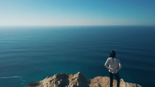 Drone view of young brave girl, sitting on the edge of a cliff