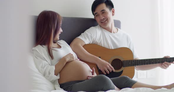 Asian husband and pregnant wife spend time together in the bedroom.