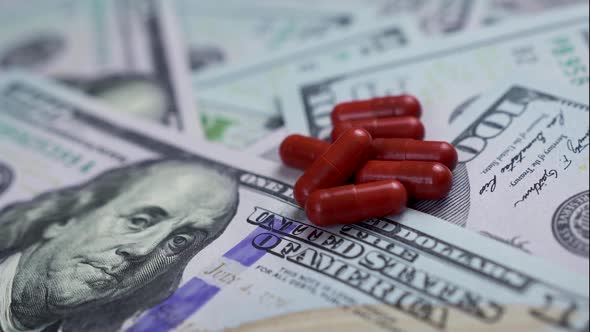 A pile of red pills, capsules, lie on the one hundred dollar bills scattered on the table alt