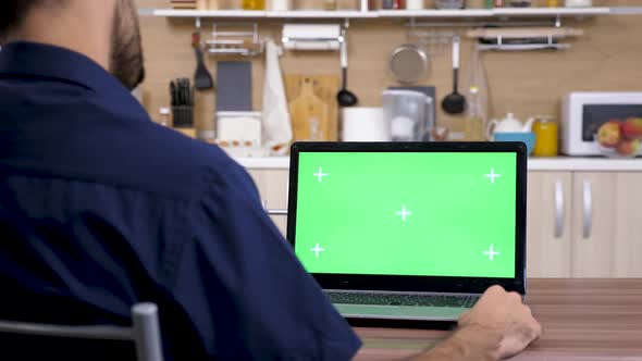 Man In The Kitchen Looking At Computer With Green Screen  alt