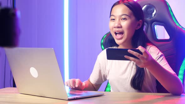 Asian Kid Girl Hold Phone And Read Comment In Laptop Then Talking To Camera While Live Stream alt