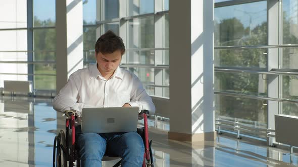 Disabled Businessman on a Wheelchair at a Window with a Laptop