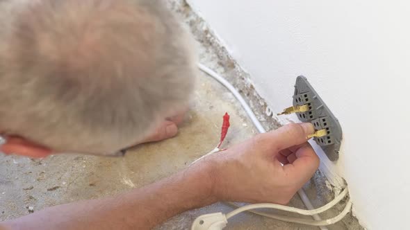 A Male Electrician Makes Electrical Wiring in the Wall Screwing the Wires and the Socket to the Wall