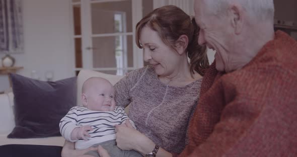 Senior couple embracing grandchild on sofa at home, multi generation togetherness