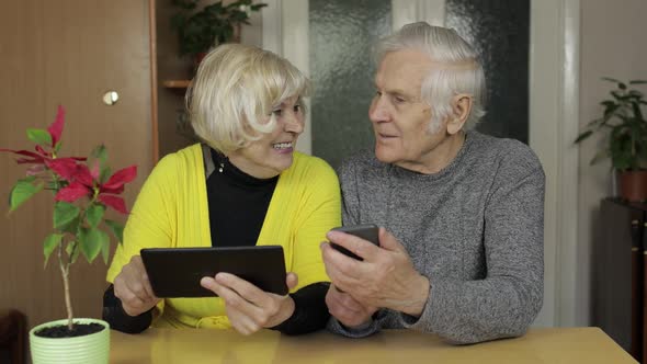 Pretty Mature Senior Couple Grandparents Enjoy Online Shopping on Phone, Tablet alt