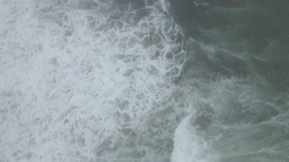 White waves crash against a rocky jagged fog shrouded coastline, aerial reveal alt