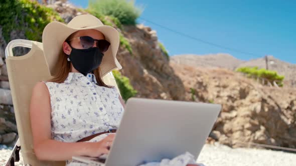 Woman in Mask Works Using Laptop on Sea Beach Sunbed in Summer