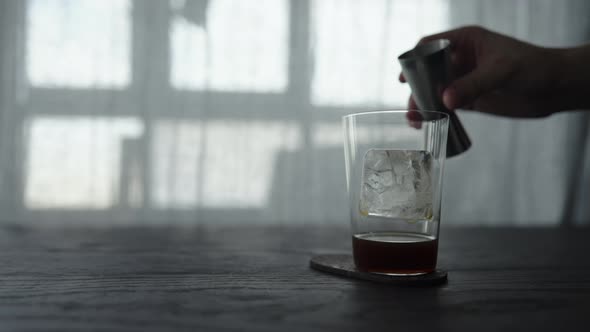 Slow Motion Pour Cold Brew Coffee Over Ice Cube in Tumbler Glass on Wood Table alt