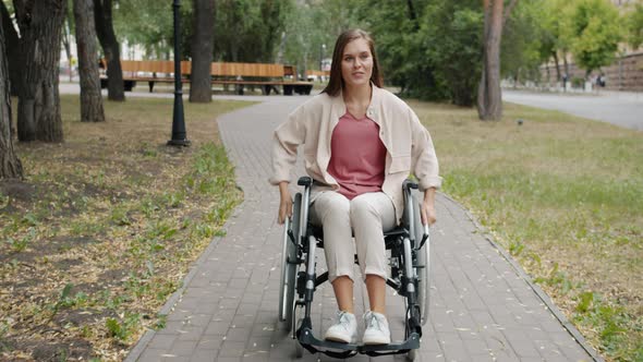 Slow Motion of Cheerful Paraplegic Girl Riding Wheelchair and Smiling in Autumn Park alt