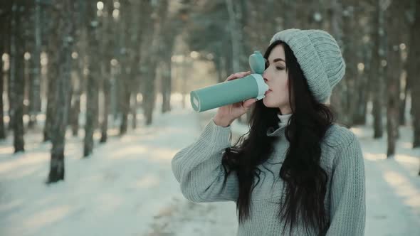 Woman in Sweater and Hat Drinks Hot Tea in Winter Forest