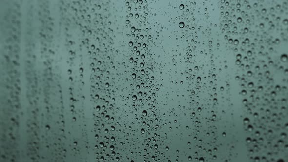 Close-up of water droplets on glass, Raindrops strike a window pane at twilight.