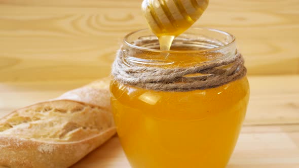 Thick Viscous Honey is Taken Out of a Glass Jar with a Wooden Spoon