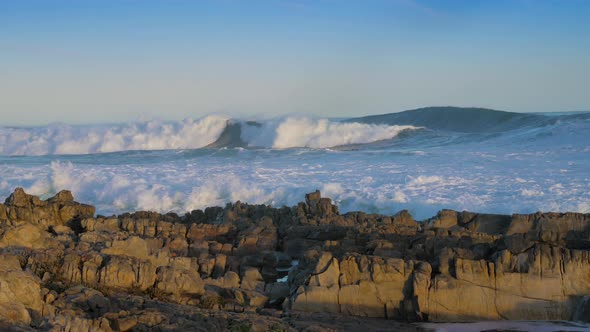 Huge waves rolling in onto rocky coastline, blue skies. alt